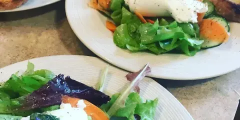 A close-up of a plated gourmet salad featuring mixed greens, burrata cheese, and fresh vegetables.