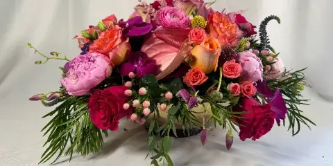 A colorful floral arrangement featuring roses, peonies, orchids, and greenery in a vase on a white background.