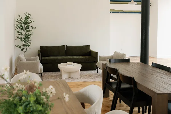 Interior view of a modern rental space featuring a green sofa, dining table, and natural light.
