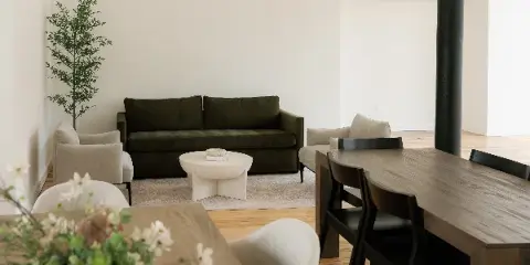 Interior view of a modern rental space featuring a green sofa, dining table, and natural light.