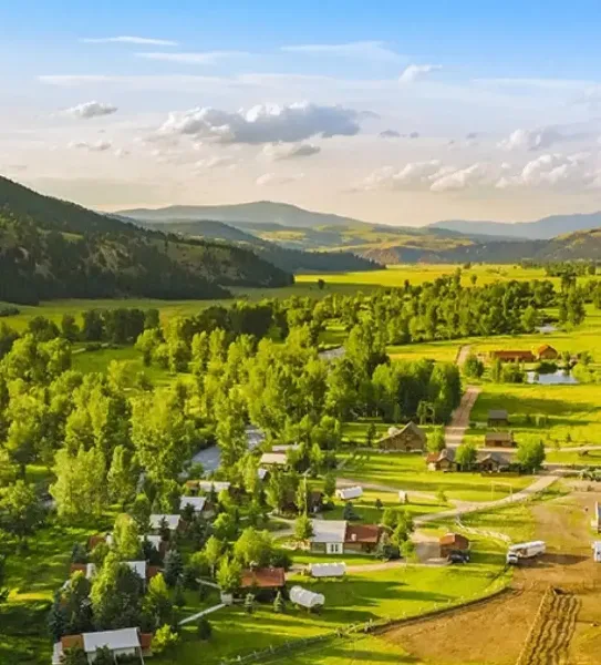 Aerial view of The Ranch at Rock Creek resort, showing multiple cabins nestled in a green valley with mountains in the background.
