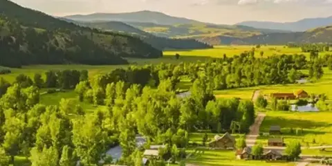 Aerial view of The Ranch at Rock Creek resort, showing multiple cabins nestled in a green valley with mountains in the background.