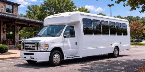 A white passenger minibus parked in a lot near a stone building.