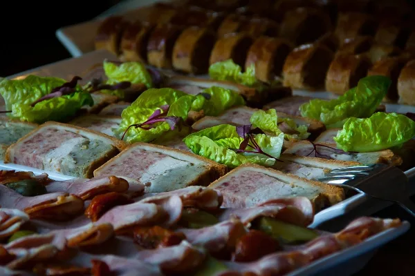 A catering platter featuring sliced meat terrines, fresh green lettuce, and bread rolls.