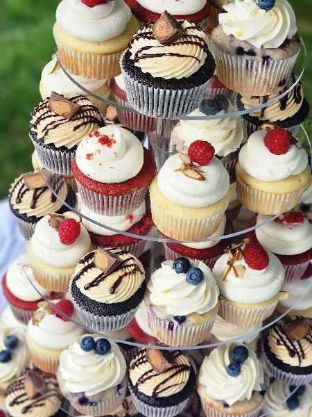 A tiered stand filled with assorted decorated cupcakes topped with berries, chocolate, and frosting.