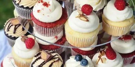 A tiered stand filled with assorted decorated cupcakes topped with berries, chocolate, and frosting.