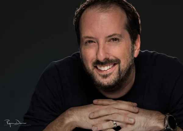 Professional portrait of a smiling man with a beard, wearing a dark shirt, with the Ryan Dinan Photography signature in the corner.