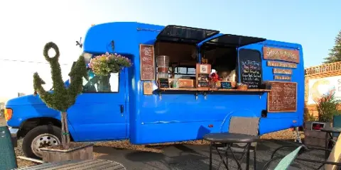 A blue food truck with an open service window, menu boards, and outdoor seating.