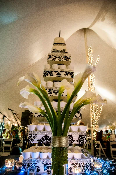 White calla lilies in a vase serving as a centerpiece in front of a tiered wedding cake stand.
