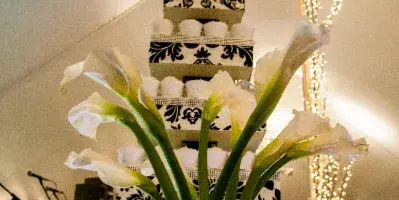 White calla lilies in a vase serving as a centerpiece in front of a tiered wedding cake stand.
