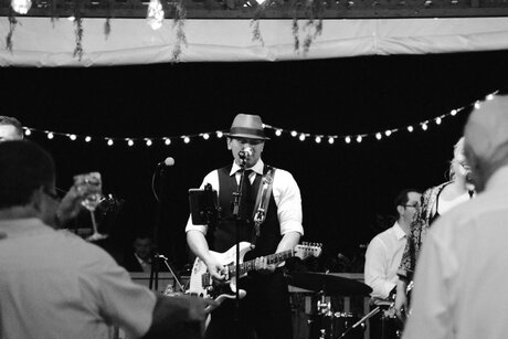 A musician wearing a hat performs on stage with a band during an event.