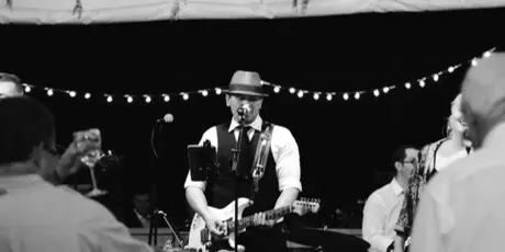 A musician wearing a hat performs on stage with a band during an event.