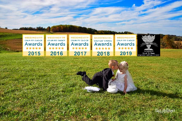 Two children in wedding costumes sitting on a grassy field with award badges overlaid.