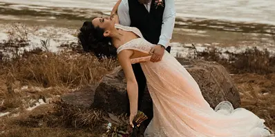 A bride and groom posing in a romantic outdoor setting with a circle of lit candles on the ground.