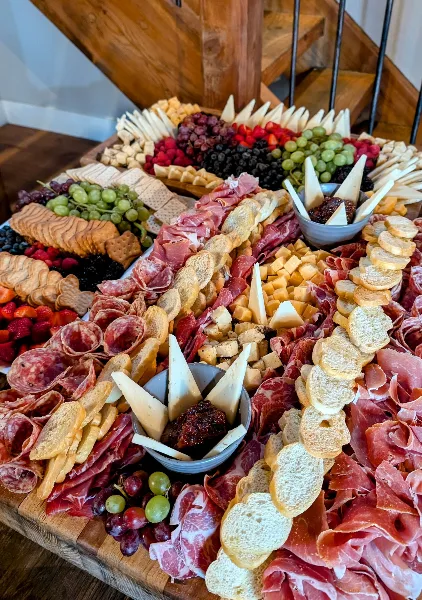 A large, elaborate charcuterie board featuring an assortment of cured meats, cheeses, fresh fruits, and breads arranged on a wooden surface.