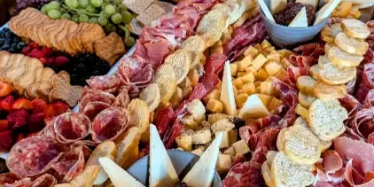 A large, elaborate charcuterie board featuring an assortment of cured meats, cheeses, fresh fruits, and breads arranged on a wooden surface.
