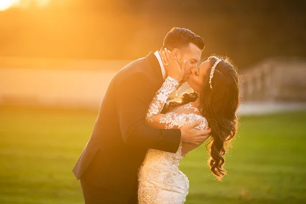 A bride and groom kissing in a field during golden hour.