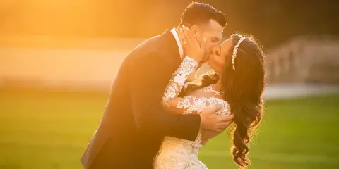 A bride and groom kissing in a field during golden hour.