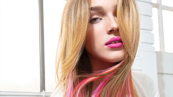 Close-up portrait of a woman with styled blonde hair featuring pink highlights and bright pink lipstick.