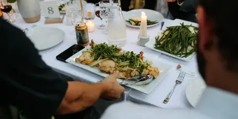 A caterer serving a plated meal of roasted chicken and green beans to guests at a formal event table.