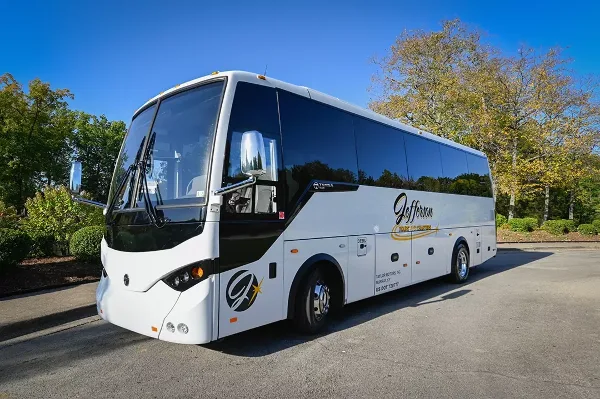 A white and black Jefferson Tours charter bus parked in a lot with trees and a blue sky.