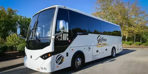 A white and black Jefferson Tours charter bus parked in a lot with trees and a blue sky.
