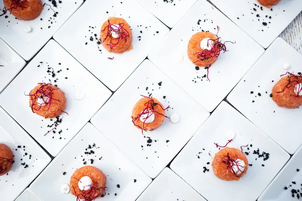 Overhead view of plated tuna tartare canapés garnished with microgreens and black caviar on white square plates.