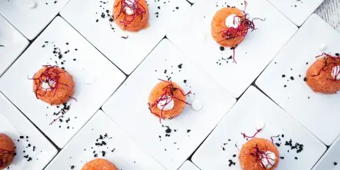 Overhead view of plated tuna tartare canapés garnished with microgreens and black caviar on white square plates.