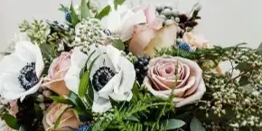 A hand holding a lush bridal bouquet with pink roses, white anemones, and greenery.