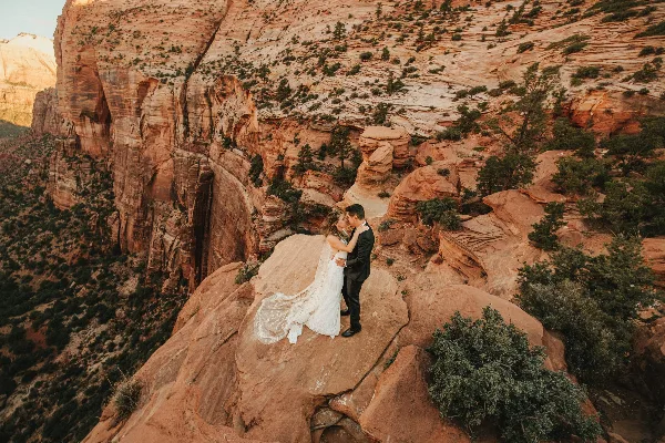 A bride and groom embracing on a rocky cliff in a desert landscape.