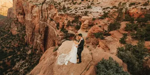A bride and groom embracing on a rocky cliff in a desert landscape.