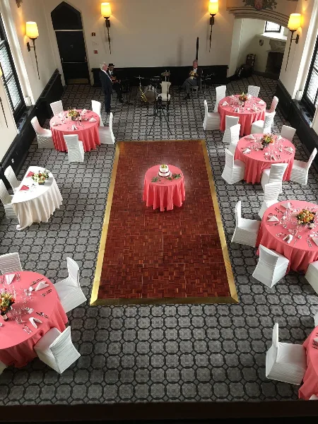 An overhead view of a wedding reception venue featuring round tables with pink tablecloths, white chairs, and a central cake table.