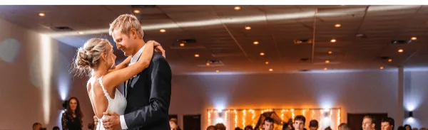 A bride and groom dancing at a wedding reception in a large indoor event venue.