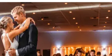 A bride and groom dancing at a wedding reception in a large indoor event venue.