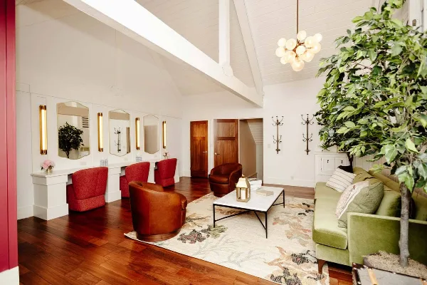 Interior view of a venue lounge featuring a green sofa, leather armchairs, a vanity with mirrors, and a large indoor tree.