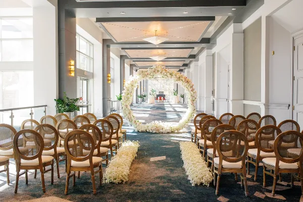 Indoor wedding ceremony setup with rows of wooden chairs and a floral arch