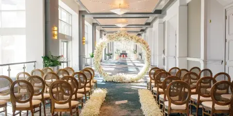 Indoor wedding ceremony setup with rows of wooden chairs and a floral arch