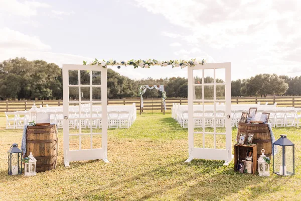 Outdoor wedding ceremony setup with white chairs, a floral arch, and a wooden fence at a farm venue.