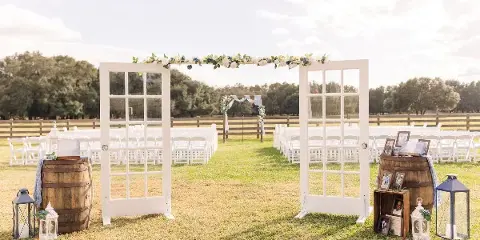 Outdoor wedding ceremony setup with white chairs, a floral arch, and a wooden fence at a farm venue.
