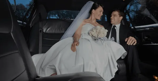 A bride and groom sitting in the back seat of a luxury car.