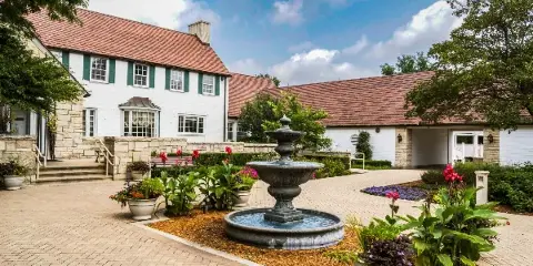 Exterior view of the Danada House historic mansion featuring a white facade, red roof, and a central stone fountain in a paved garden courtyard.