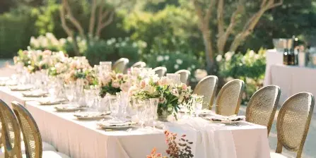 An outdoor wedding reception table with a long white runner, glassware, and lush, organic floral centerpieces and floor arrangements.