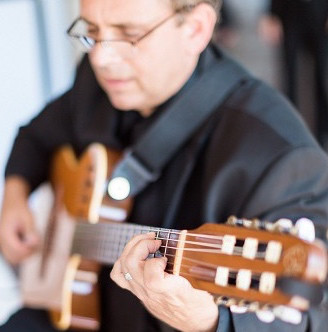 A musician wearing glasses and a black shirt playing a classical guitar.