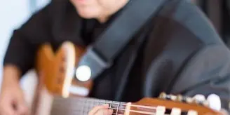 A musician wearing glasses and a black shirt playing a classical guitar.