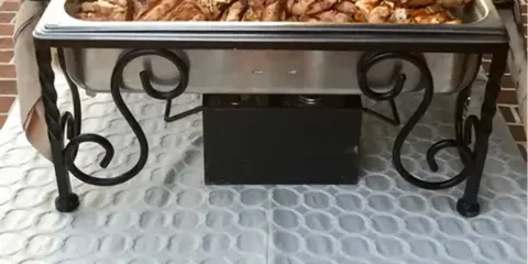 A catering station featuring two chafing dishes filled with grilled meats and a tray of dipping sauces.