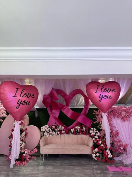 Decorated event space with a pink sofa, floral arrangements, and heart-shaped balloons.