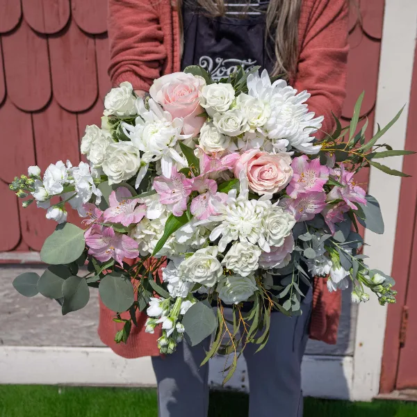 A person in a Vogt's apron holding a large bridal bouquet of white roses, pink alstroemeria, and greenery.