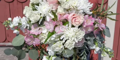 A person in a Vogt's apron holding a large bridal bouquet of white roses, pink alstroemeria, and greenery.