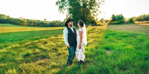A bride and groom standing in a grassy field at a wedding venue.