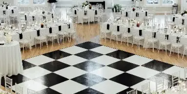 A wedding reception hall set up with white tables, chairs, and a large black-and-white checkered dance floor.
